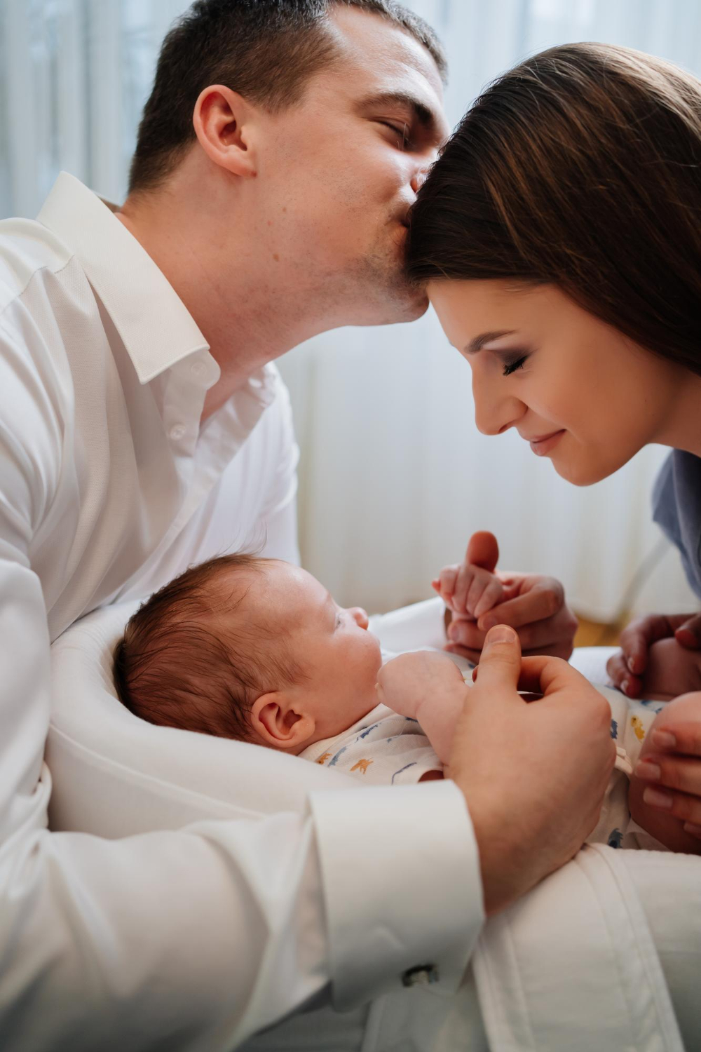 uomo che bacia donna sulla fronte e tiene le mani del loro bambino appena nato